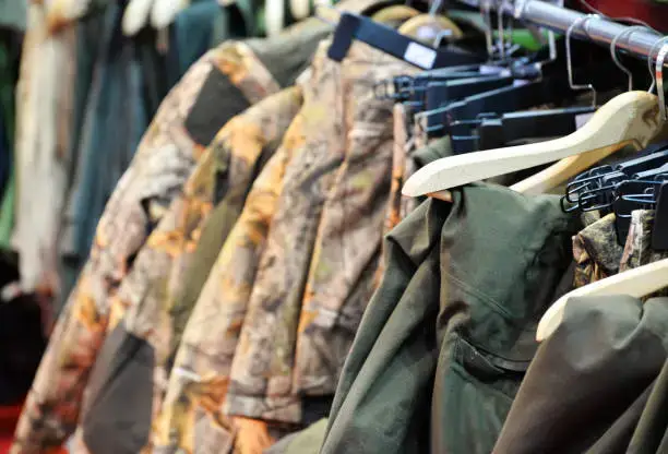 Rack of military clothing, including camouflage jackets, hanging on display.