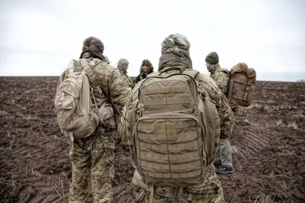 Army soldiers carrying military backpacks on muddy terrain