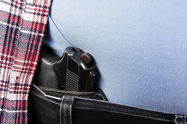 pistolet ukryty w pasie pary czarnych dżinsów i czerwonej flanelowej koszuli w kratę