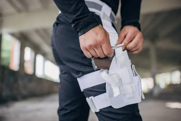 A person wearing a drop-leg holster with a firearm, adjusting the holster on their thigh