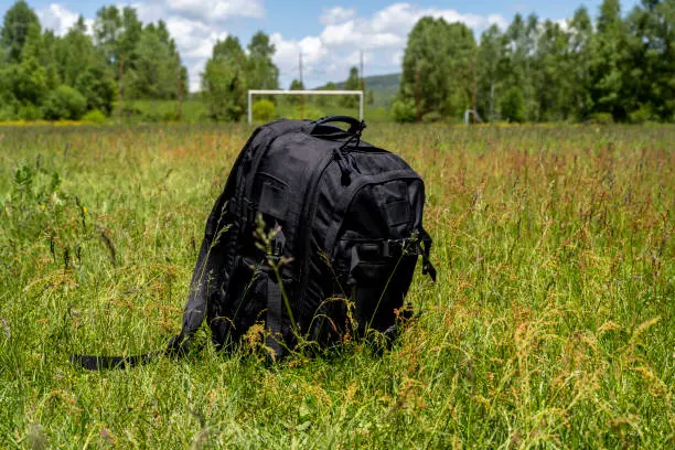Black backpack left on the grass meadow.
