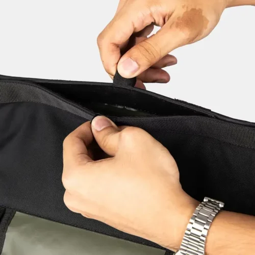 Manos abriendo un bolsillo interior con cremallera de la mochila táctica negra.