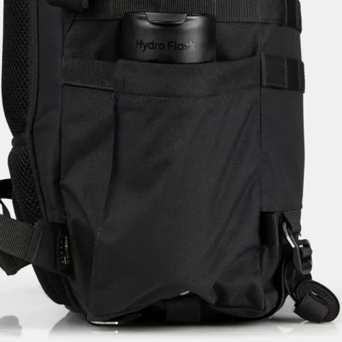Bolsillo lateral de una mochila táctica negra que contiene una botella Hydro Flask.